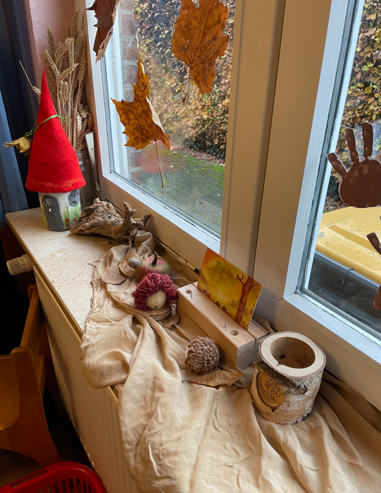 Fensterbank mit herbstlichen Dekorationen, wie Blättern, einem gefilzten Häuschen und Naturmaterialien.