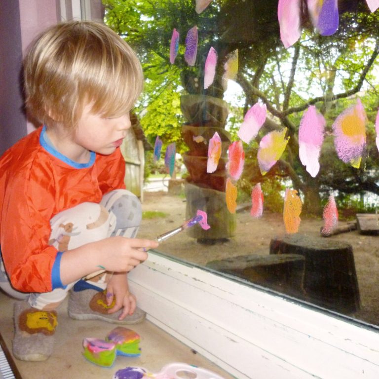 Ein Kind malt farbige Punkte auf ein Fenster mit einem Pinsel.