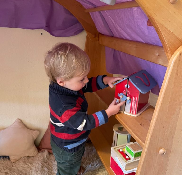 Kleiner Junge spielt unter einem Spielbogen, der mit Tüchern behangen ist.
